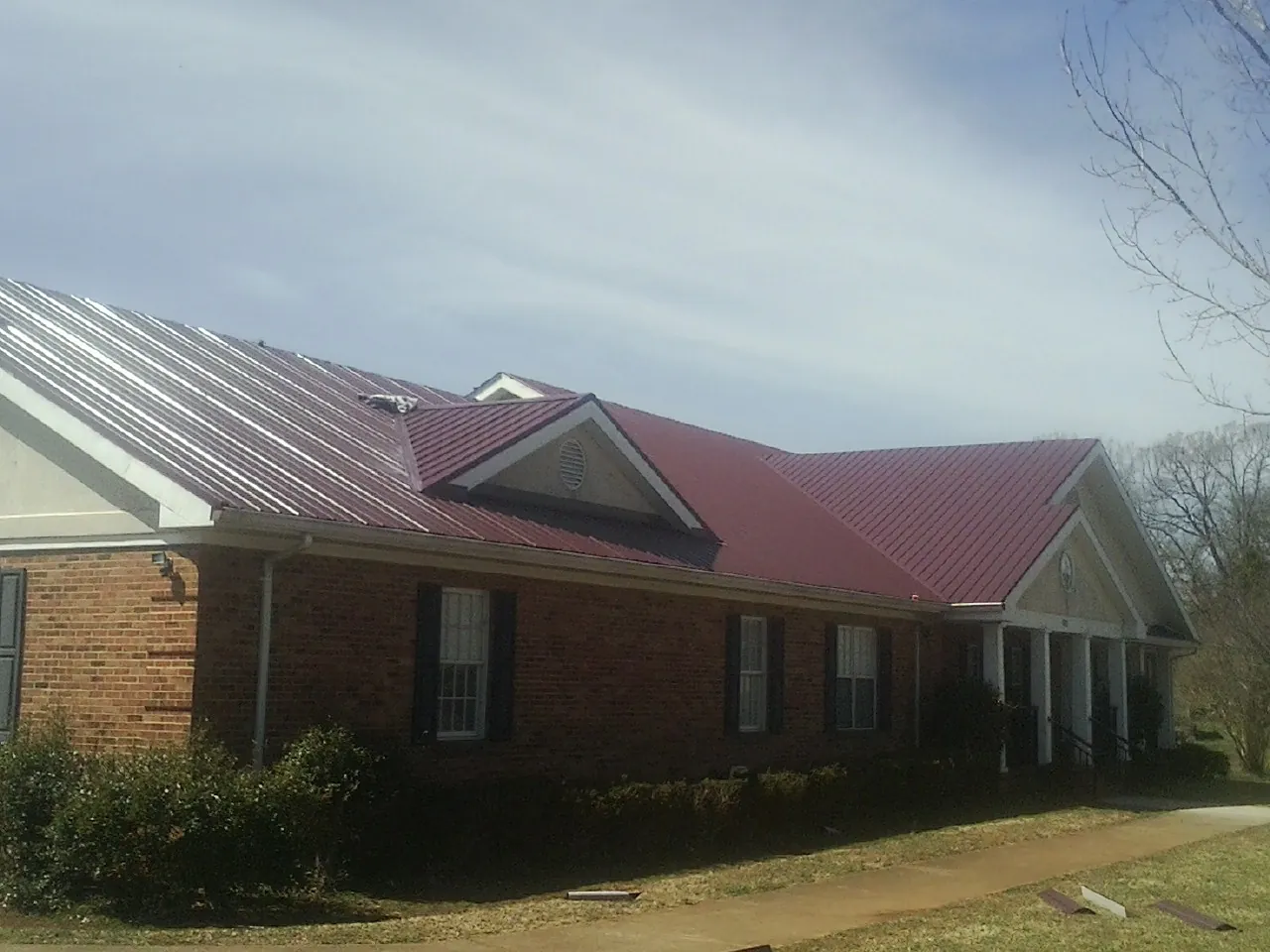 Red metal roof with gabled entries on a long brick building, from a Hail Damage Roof Repair job in Moab
